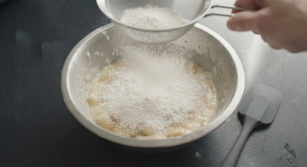 Tamizando harina y levadura sobre la masa de pan de plátano