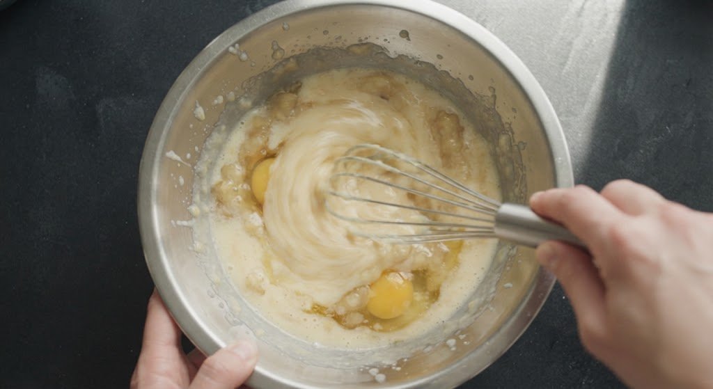 Mezclando plátano machacado con huevo, azúcar y aceite en un bol