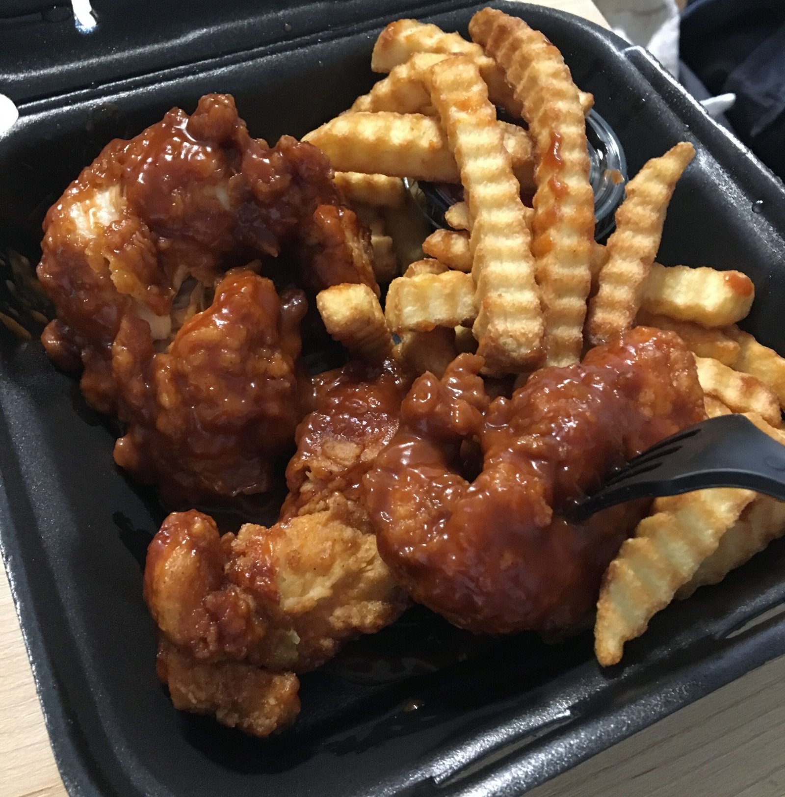 Boneless de pollo con salsa barbacoa y patatas onduladas en un envase para llevar (foto de archivo)