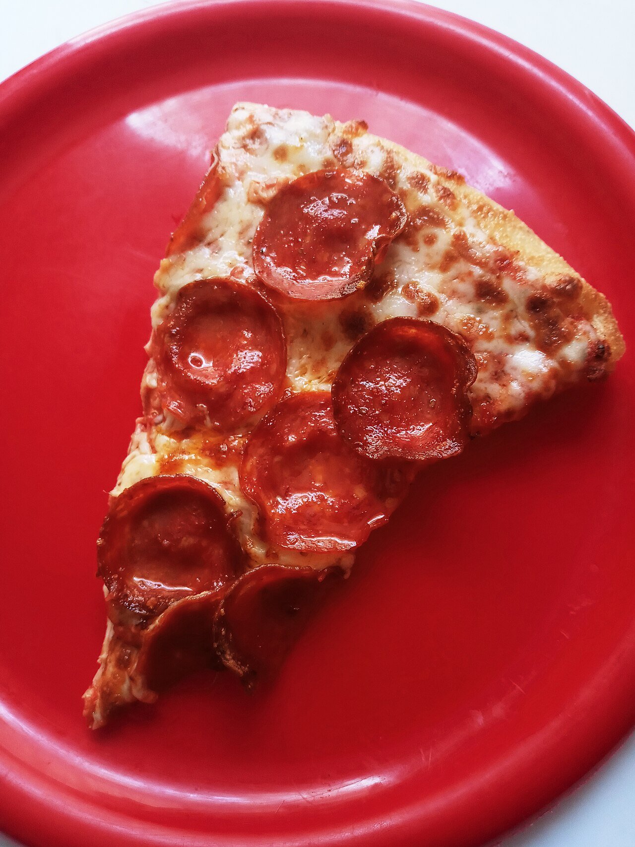 Porción de pizza de pepperoni en un plato rojo